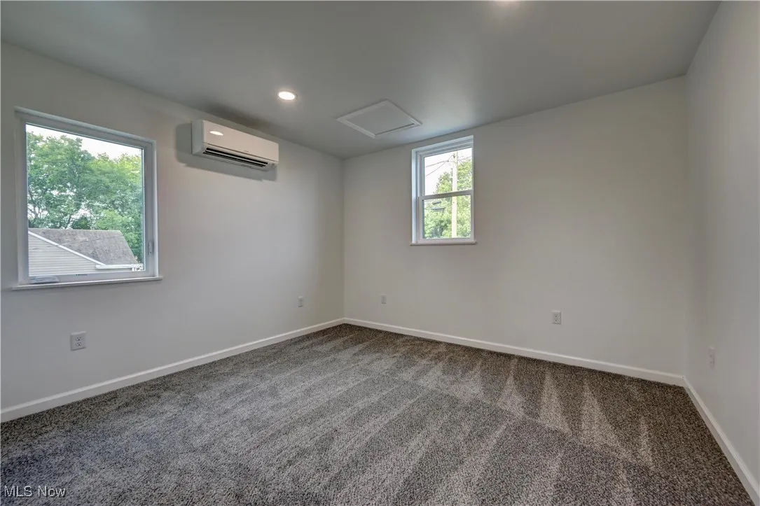 Spare room with attic access, dark carpet, a wall unit AC, and recessed lighting