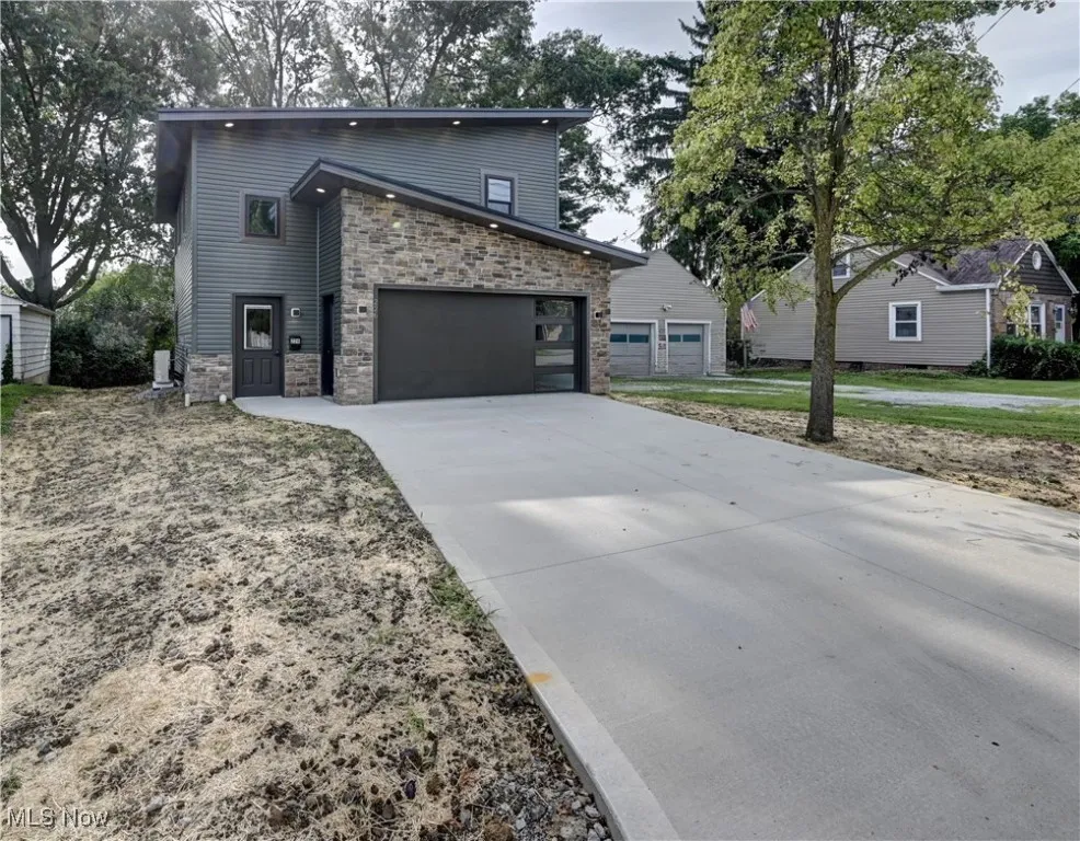 Contemporary home with stone siding, driveway, and a garage