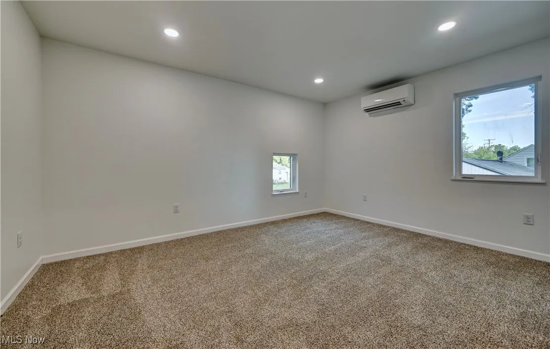 Carpeted empty room with recessed lighting and an AC wall unit