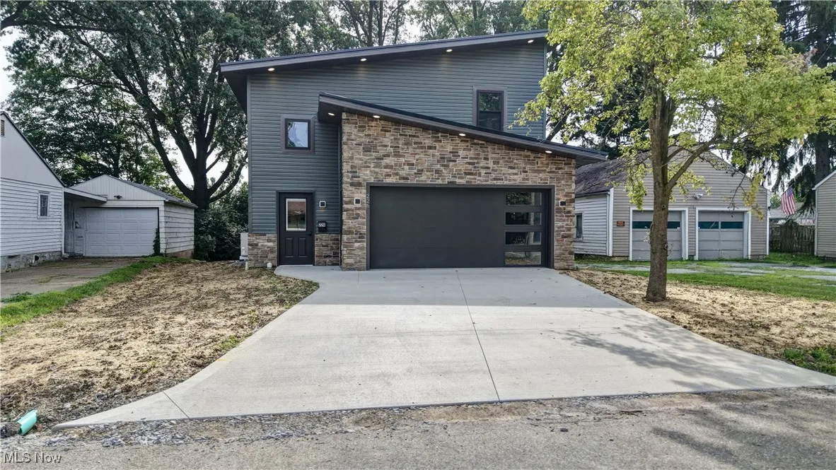 Contemporary house featuring a garage, stone siding, concrete driveway, and an outdoor structure