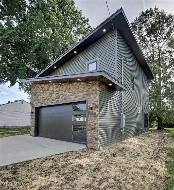 View of home's exterior with stone siding and concrete driveway