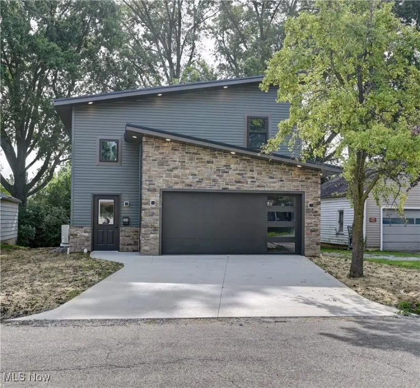 View of front of property featuring stone siding, driveway, and an attached garage