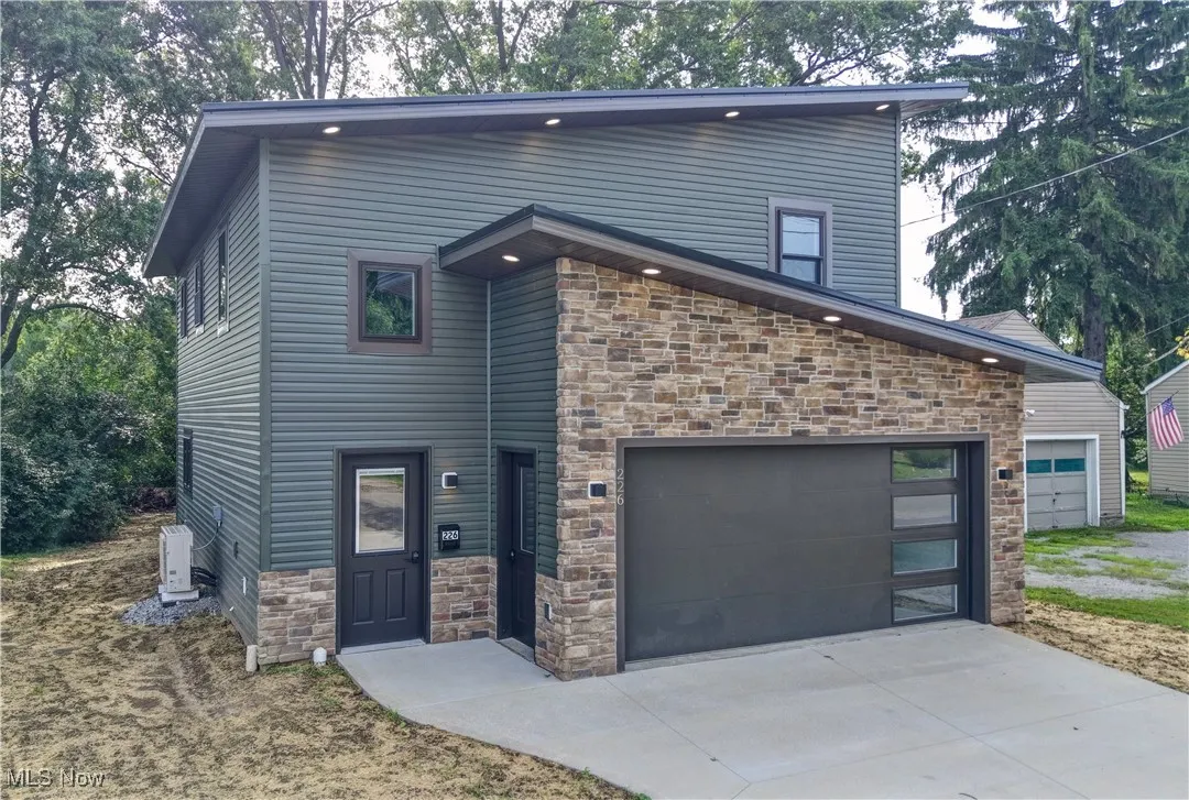 Contemporary home featuring stone siding, a garage, and driveway