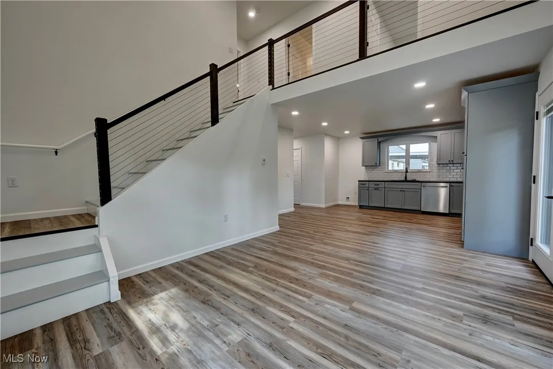 Unfurnished living room with light wood-style flooring, a high ceiling, recessed lighting, and stairs