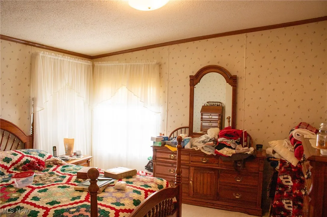 Bedroom featuring ornamental molding, a textured ceiling, and wallpapered walls