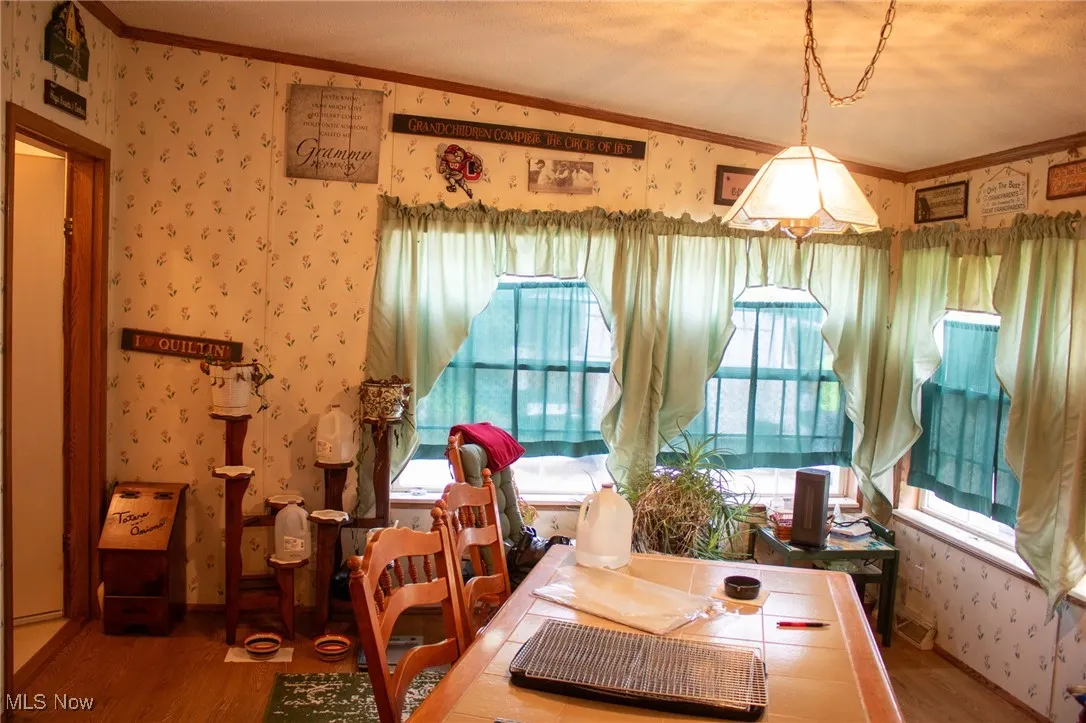 Dining space with wallpapered walls, ornamental molding, and wood finished floors