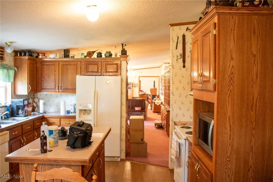 Kitchen with white appliances, light wood-style flooring, light countertops, brown cabinets, and a textured ceiling