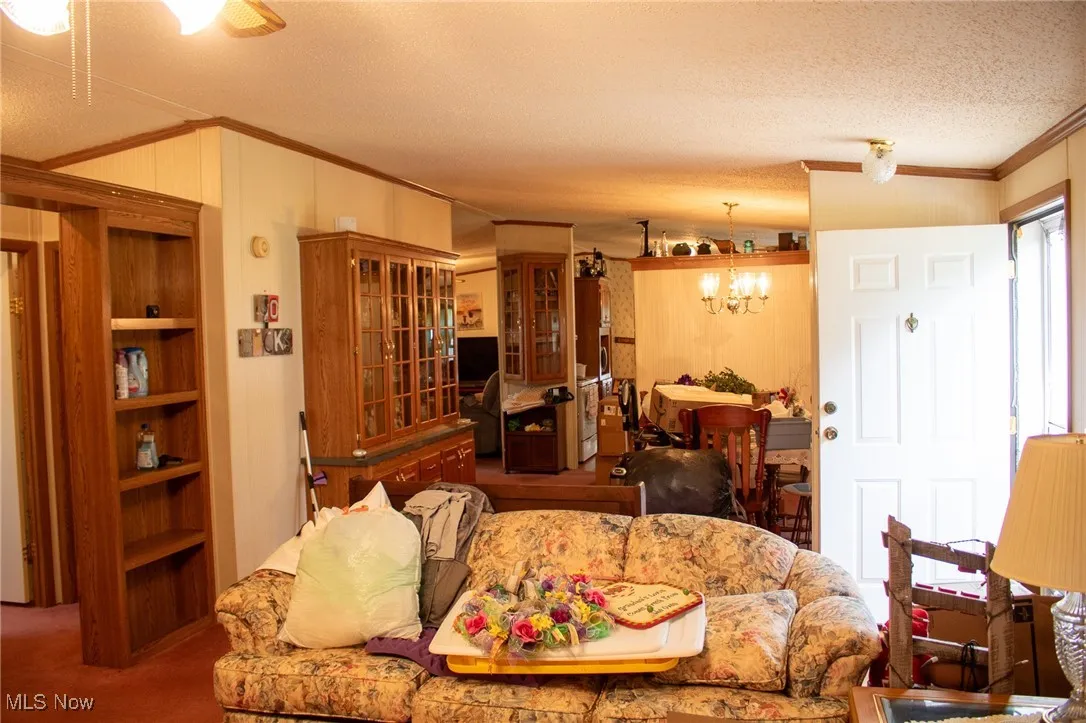 Living room featuring ornamental molding, a textured ceiling, a chandelier, and carpet floors
