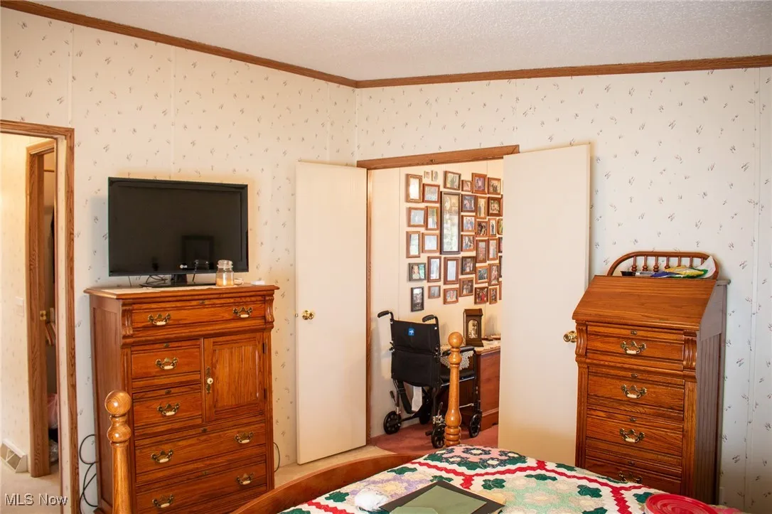 Bedroom with ornamental molding, a textured ceiling, and wallpapered walls