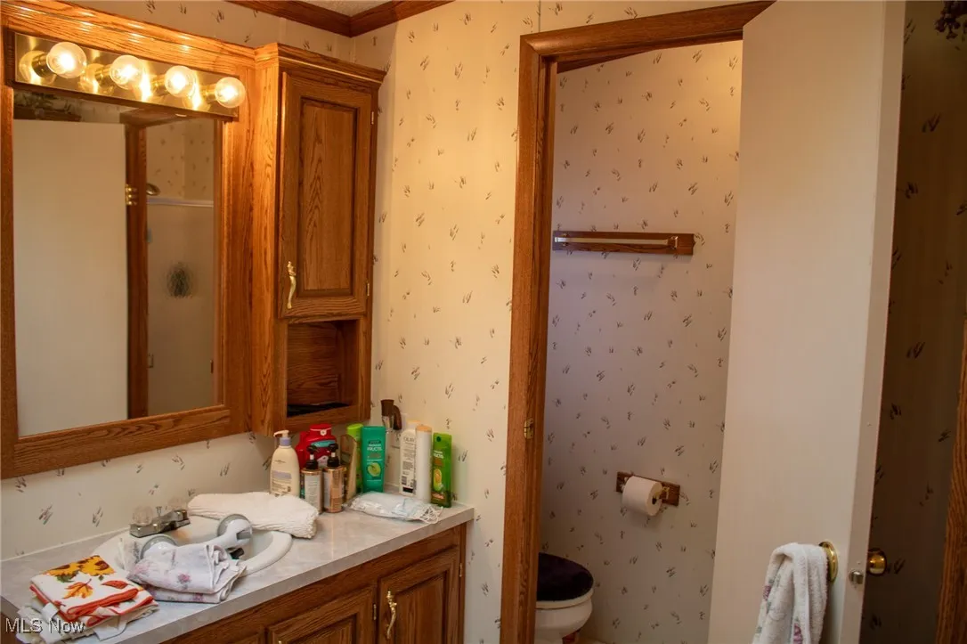 Full bath with wallpapered walls, vanity, and an enclosed shower