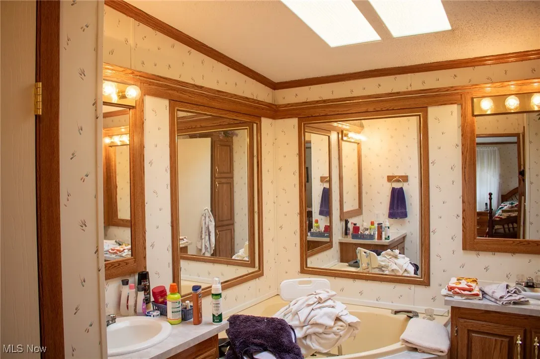Bathroom featuring vanity, crown molding, and wallpapered walls