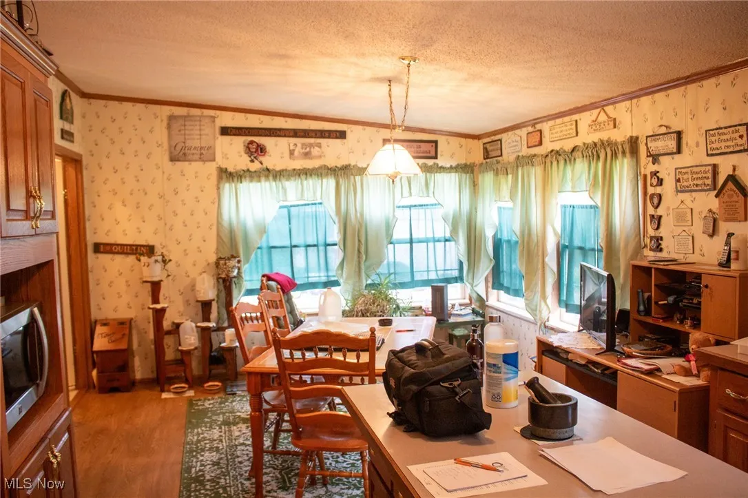 Dining room featuring crown molding, wood finished floors, wallpapered walls, a textured ceiling, and vaulted ceiling