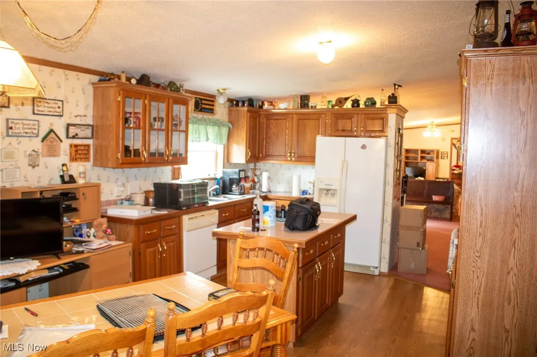 Kitchen with white appliances, a textured ceiling, brown cabinets, a center island, and glass insert cabinets