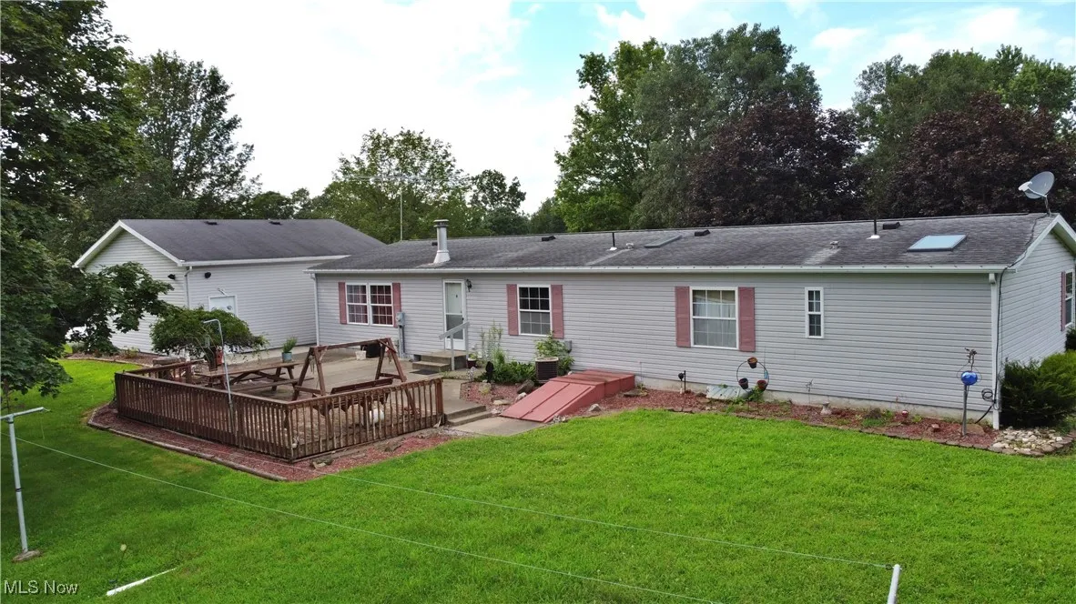 Back of property with a lawn, a deck, and a shingled roof
