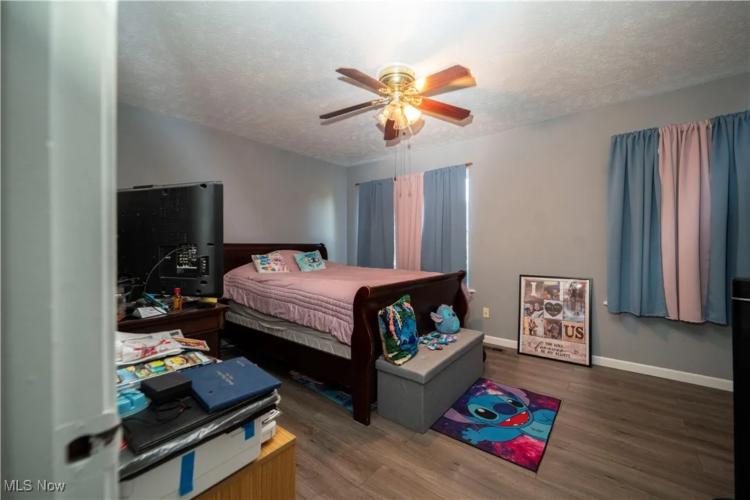 Bedroom with a textured ceiling, wood finished floors, and a ceiling fan