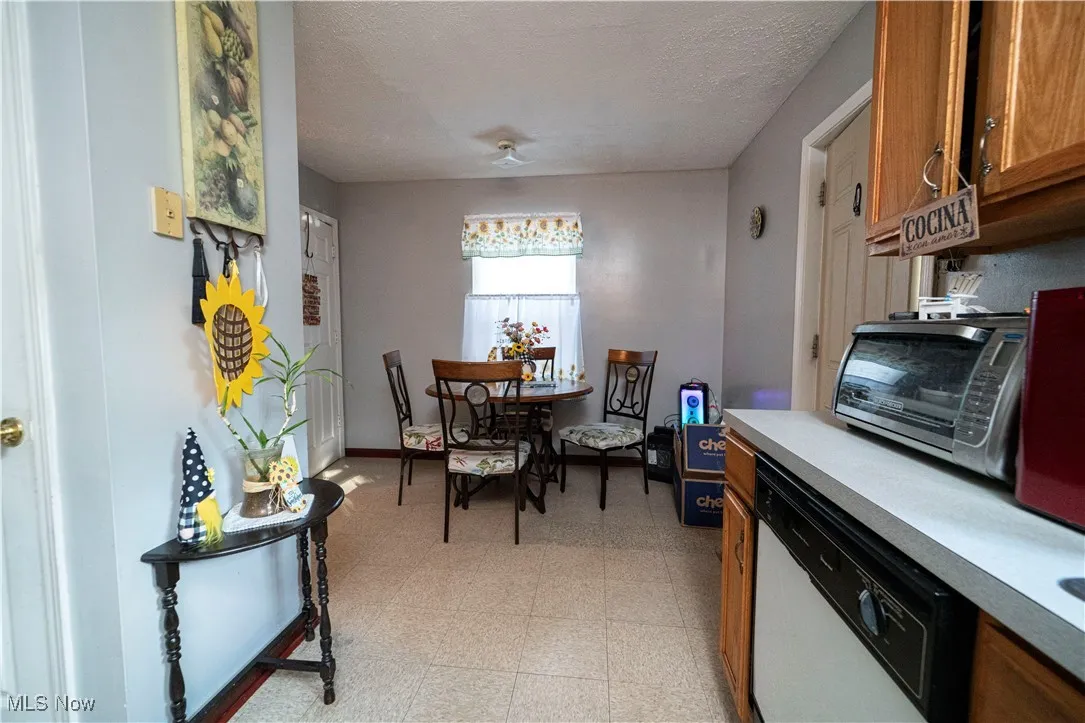 Kitchen featuring light floors, brown cabinetry, a textured ceiling, dishwasher, and light countertops
