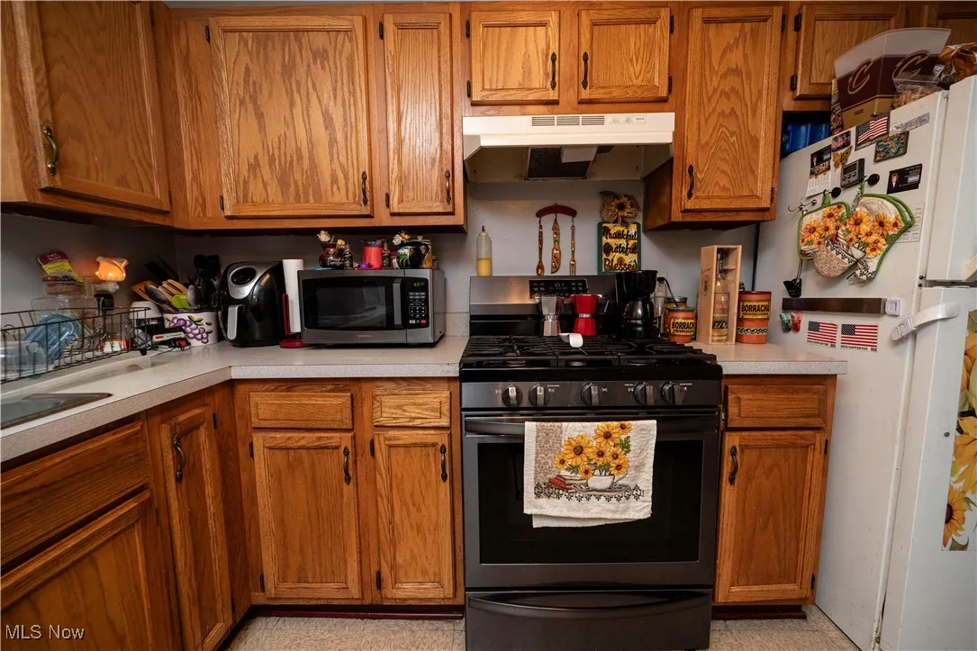 Kitchen featuring appliances with stainless steel finishes, light countertops, under cabinet range hood, and brown cabinetry