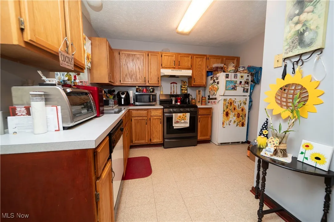 Kitchen with light flooring, stainless steel appliances, light countertops, a textured ceiling, and brown cabinets