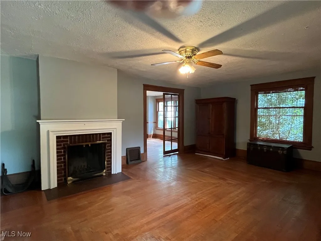 Unfurnished living room featuring a textured ceiling, wood finished floors, a fireplace, and ceiling fan