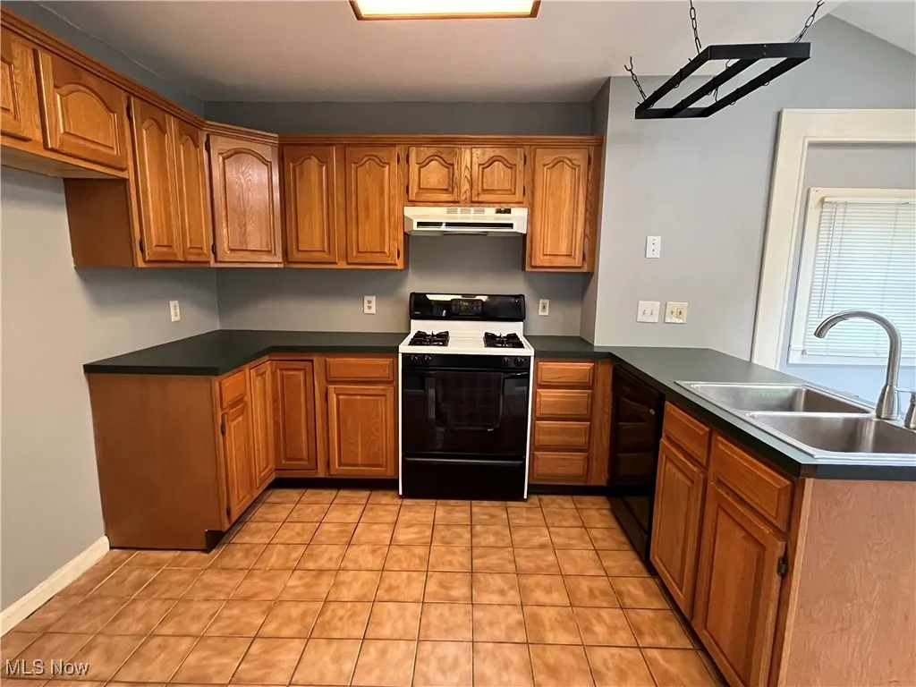 Kitchen featuring gas stove, a peninsula, brown cabinets, dishwasher, and under cabinet range hood