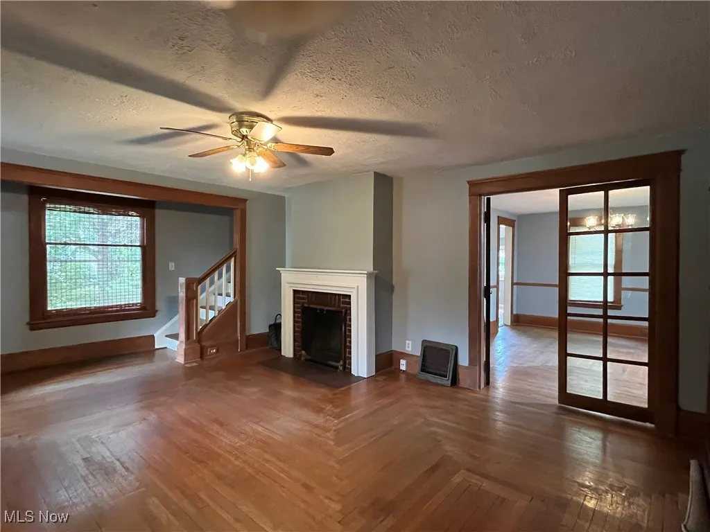 Unfurnished living room featuring stairway, a textured ceiling, a brick fireplace, hardwood / wood-style floors, and ceiling fan