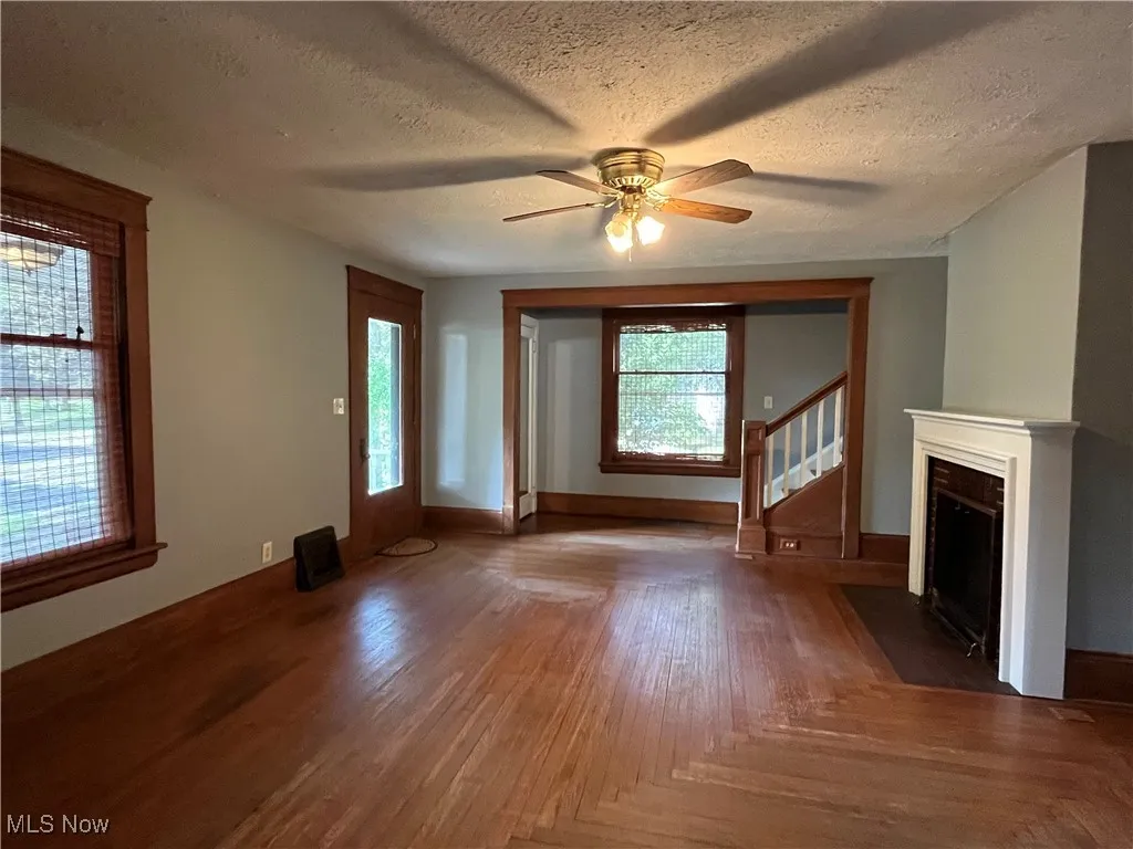Unfurnished living room featuring a textured ceiling, a ceiling fan, a fireplace with flush hearth, wood finished floors, and stairway