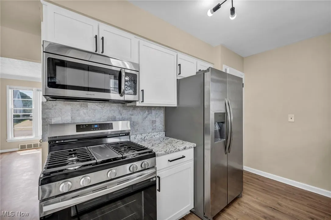 Kitchen with appliances with stainless steel finishes, white cabinetry, backsplash, light stone countertops, and wood finished floors