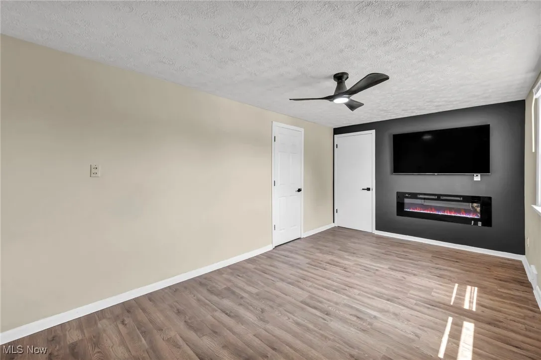  Master Bedroom featuring wood finished floors, a textured ceiling, ceiling fan, and a glass covered fireplace
