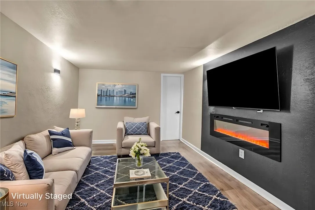 Living area featuring a textured wall, wood finished floors, and a glass covered fireplace