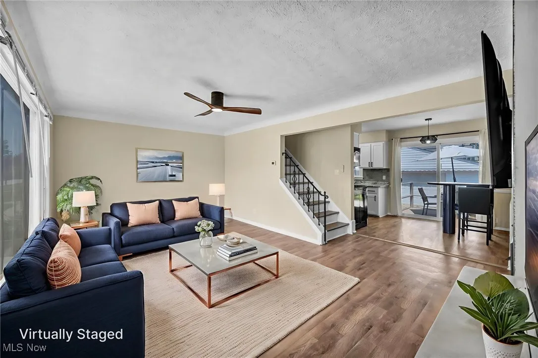 Living room with stairs, wood finished floors, ceiling fan, and a textured ceiling