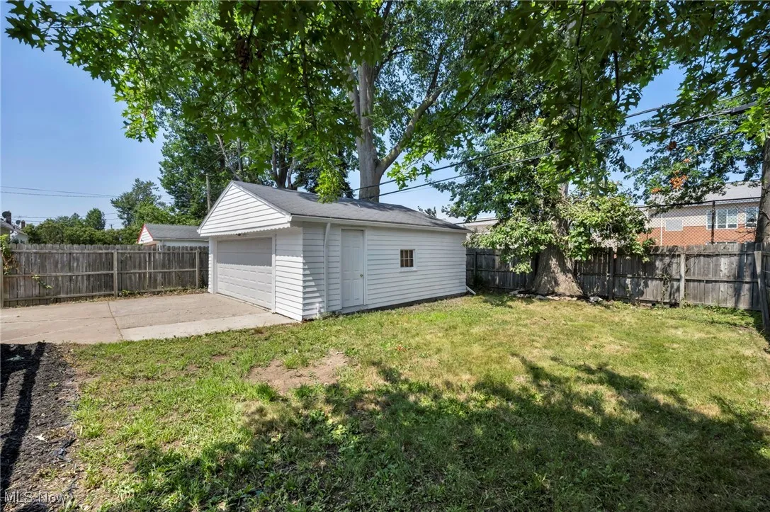 Fenced backyard with a detached garage, an outdoor structure, and a patio area