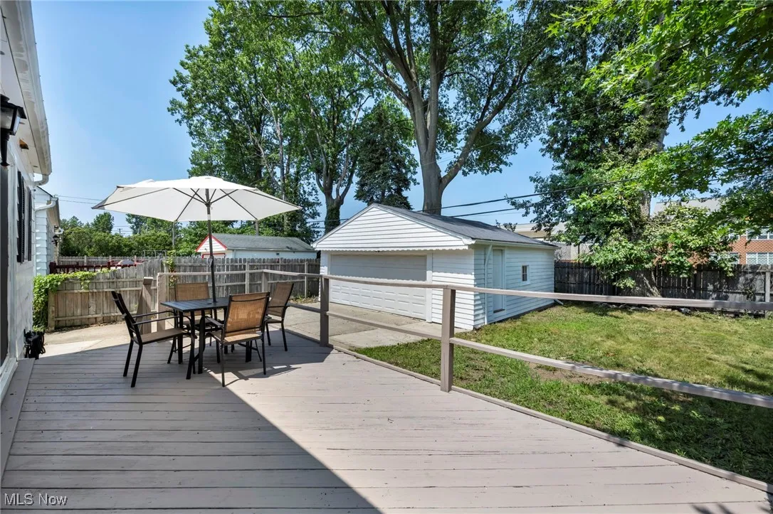 Wooden terrace with an outbuilding, a fenced backyard, outdoor dining area, and a garage