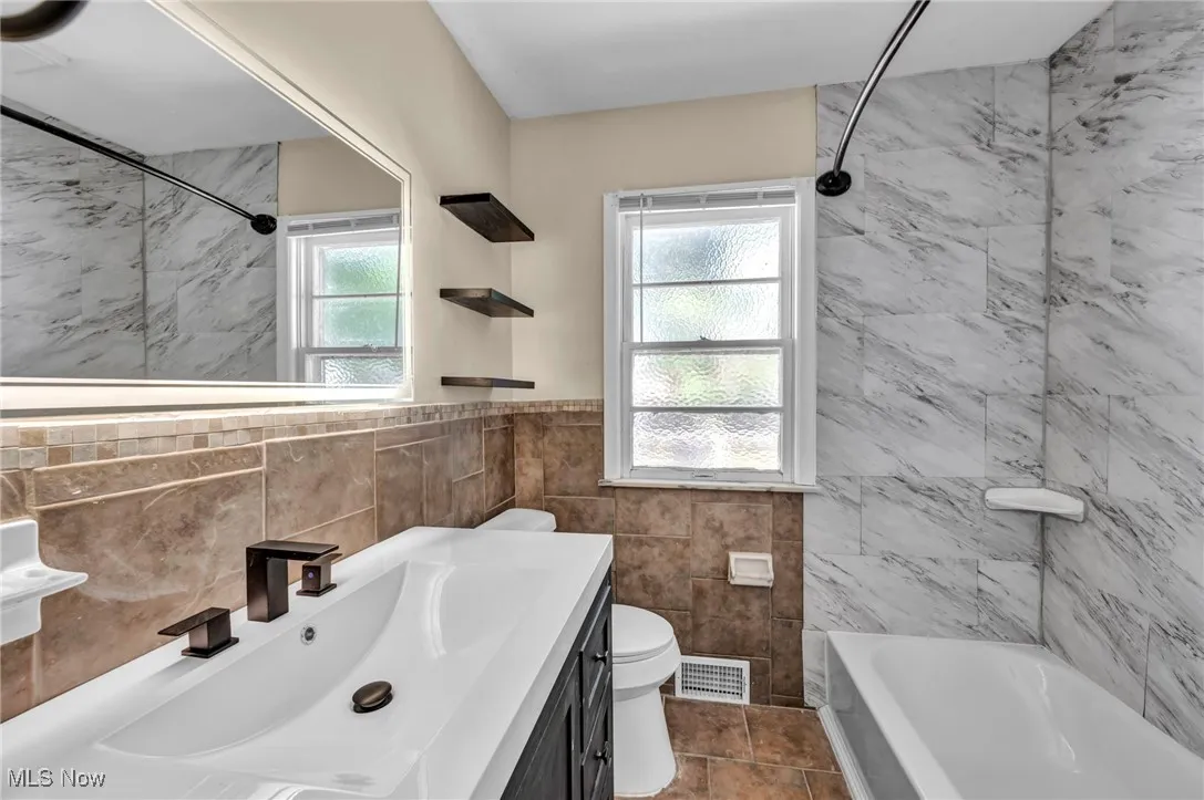 Full bath featuring tile walls, vanity, wainscoting, tile patterned floors, and  shower combination