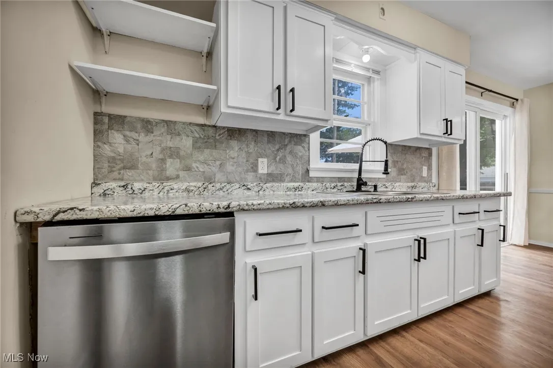 Kitchen featuring stainless steel dishwasher, backsplash, white cabinetry, wood finished floors, and light stone countertops