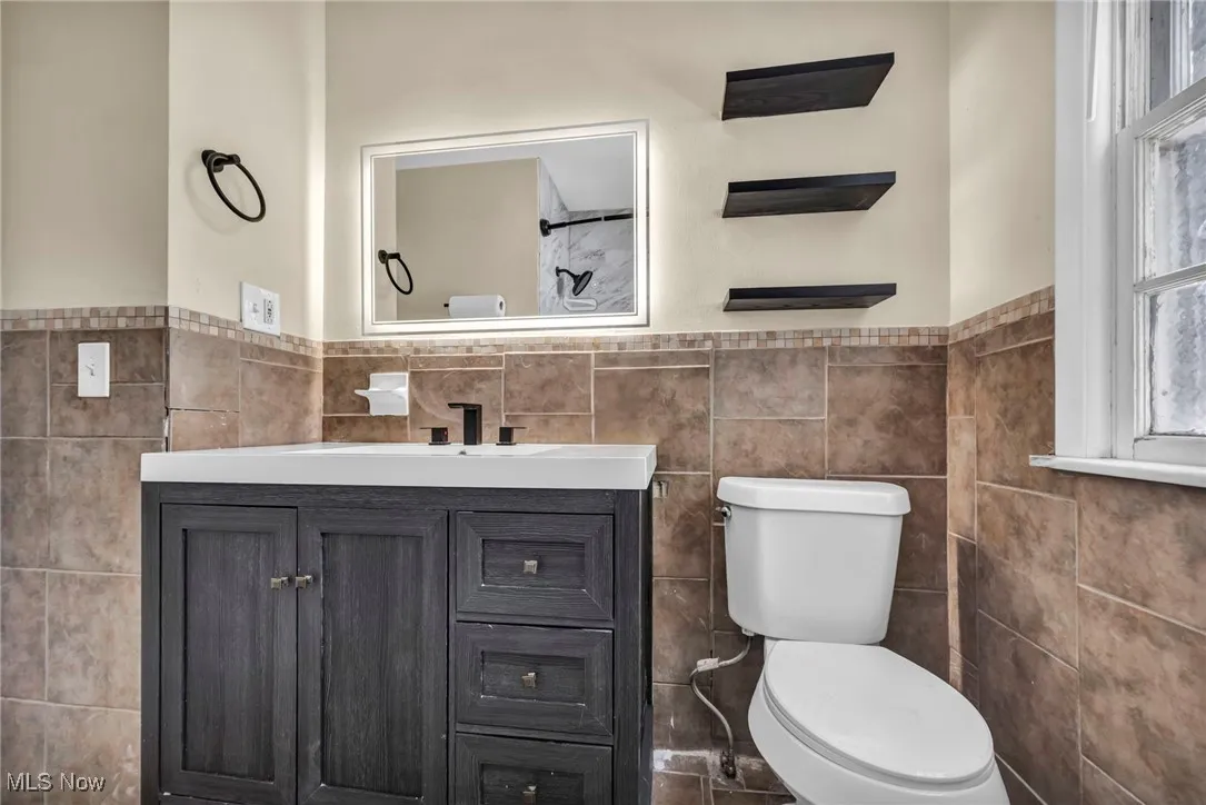 Full bathroom featuring tile walls, vanity, and a wainscoted wall
