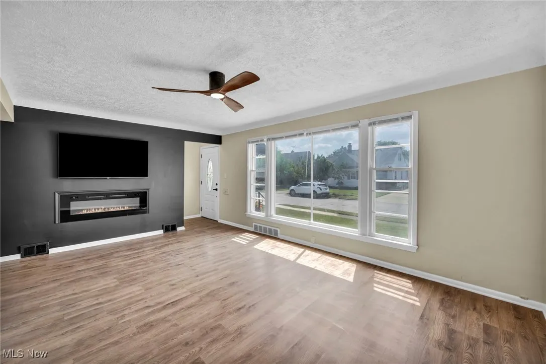 Unfurnished living room featuring a glass covered fireplace, ceiling fan, wood finished floors, and a textured ceiling