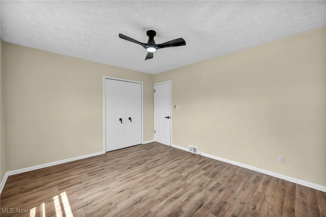 Unfurnished bedroom featuring a textured ceiling, wood finished floors, a closet, and ceiling fan