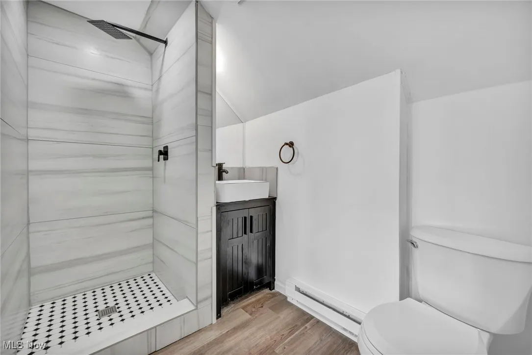Full bathroom featuring a tile shower, a baseboard radiator, wood finished floors, vanity, and vaulted ceiling