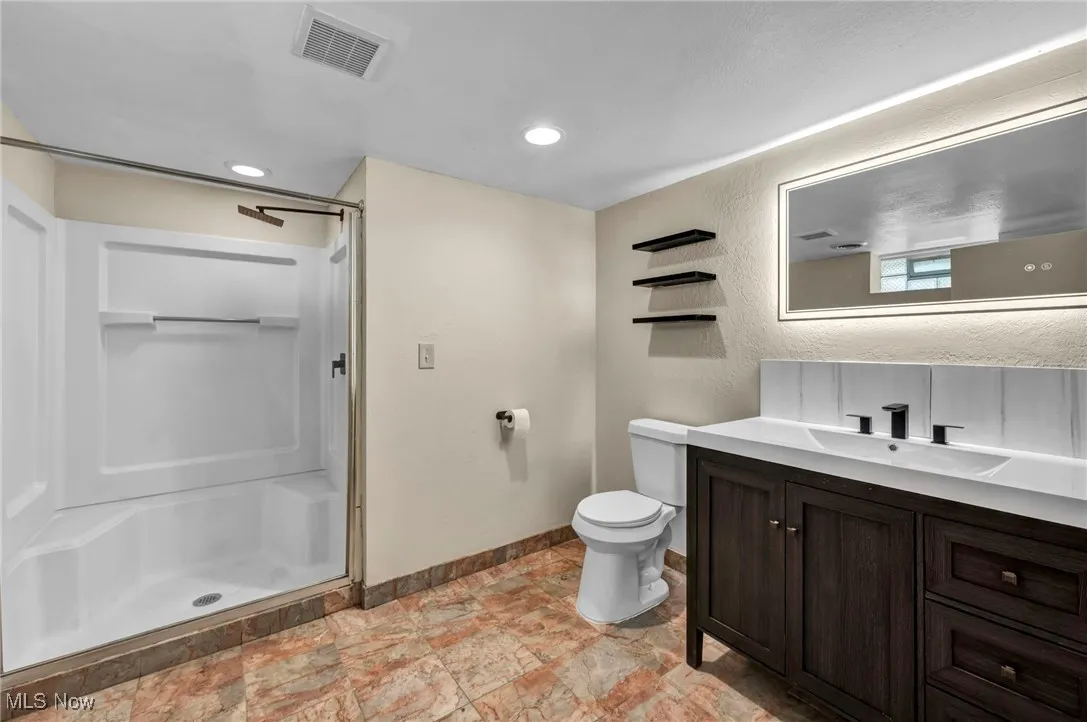 Bathroom with a shower stall, vanity, recessed lighting, and a textured wall