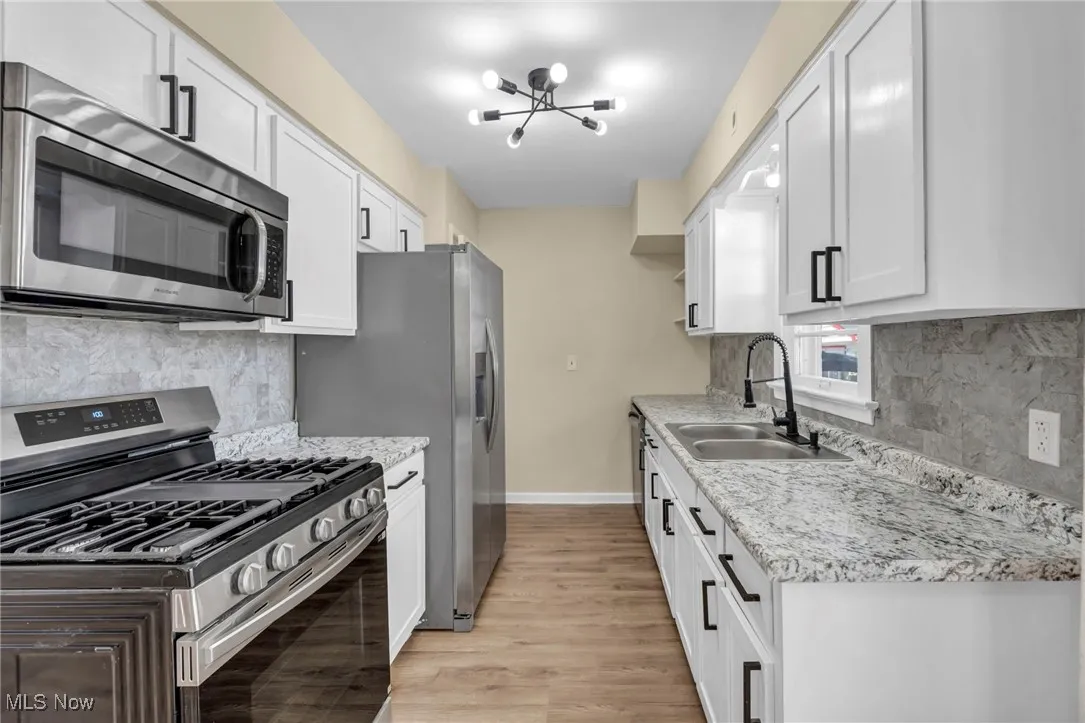 Kitchen featuring appliances with stainless steel finishes, decorative backsplash, light wood-style floors, a chandelier, and white cabinets