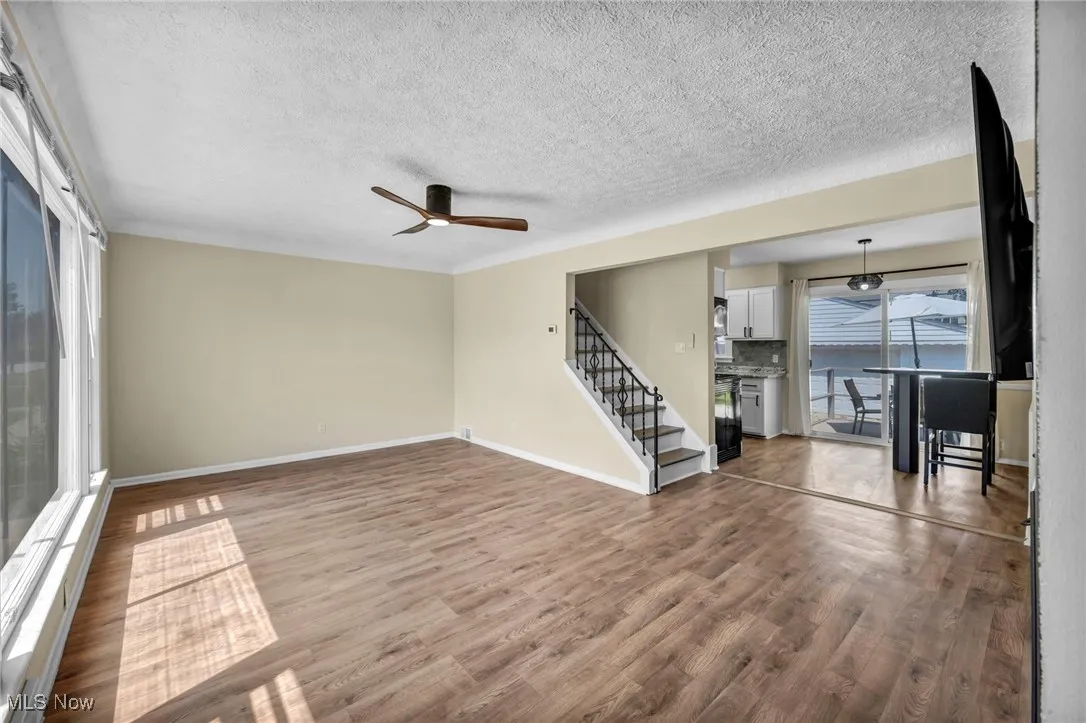 Unfurnished living room featuring stairs, wood finished floors, ceiling fan, and a textured ceiling