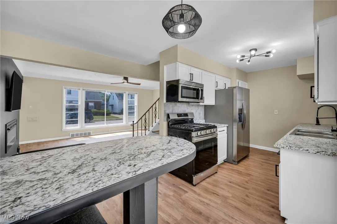 Kitchen featuring stainless steel appliances, light wood-style flooring, white cabinetry, a ceiling fan, and tasteful backsplash