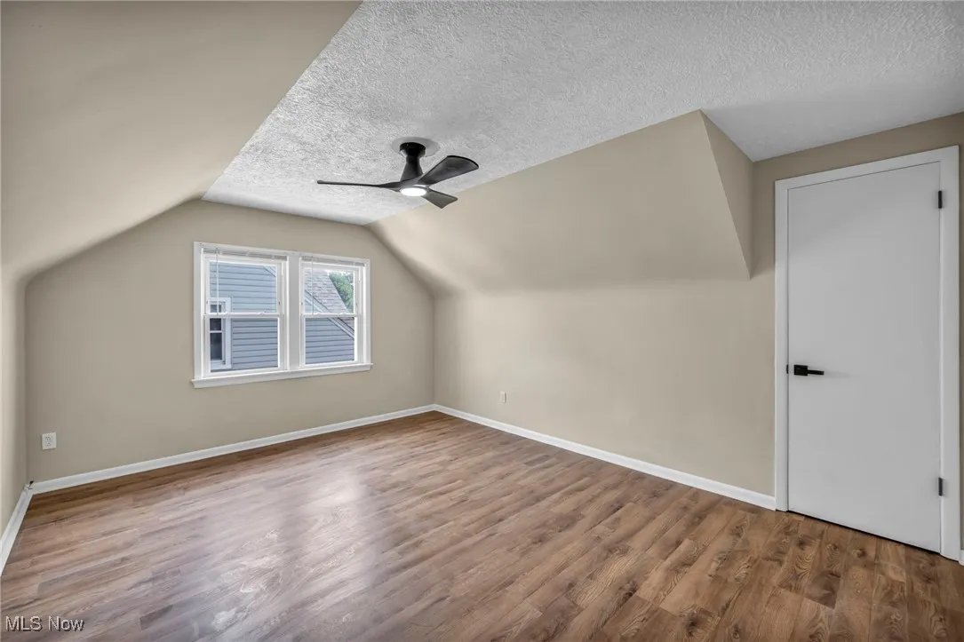 Mafeaturing wood finished floors, a textured ceiling, lofted ceiling, and a ceiling fan