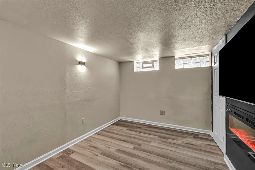 Basement with a textured ceiling, light wood-style flooring, and a textured wall