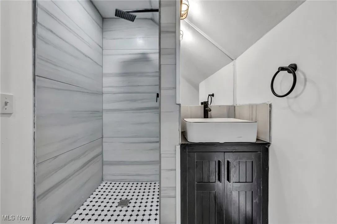Full bathroom featuring tiled shower, vanity, and lofted ceiling
