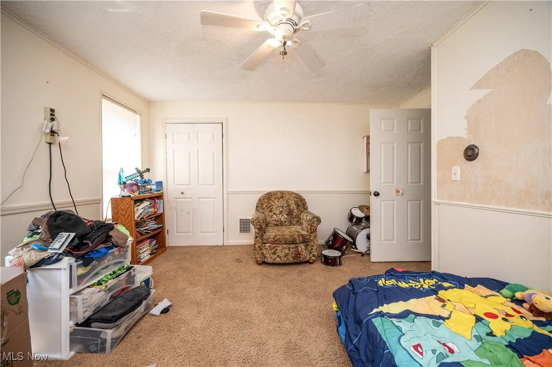 Bedroom featuring wainscoting, a textured ceiling, carpet flooring, a ceiling fan, and crown molding