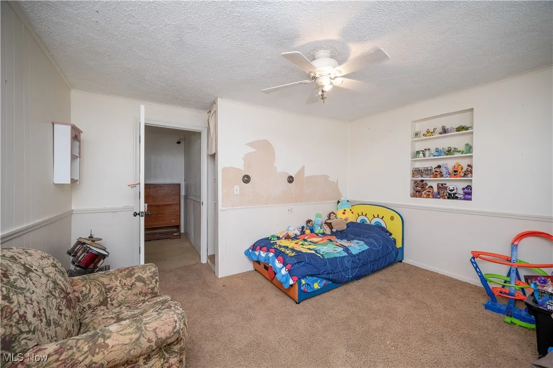Bedroom featuring a textured ceiling, carpet flooring, ornamental molding, and ceiling fan
