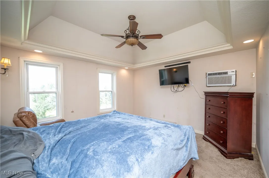 Bedroom featuring a raised ceiling, recessed lighting, light carpet, and an AC wall unit