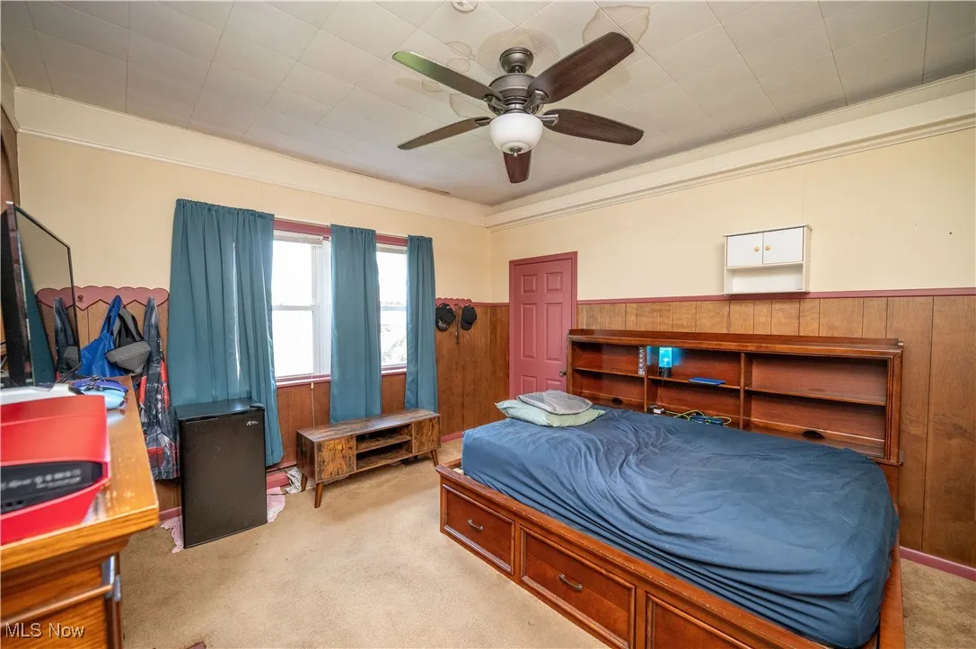 Carpeted bedroom with a wainscoted wall, wood walls, and ceiling fan