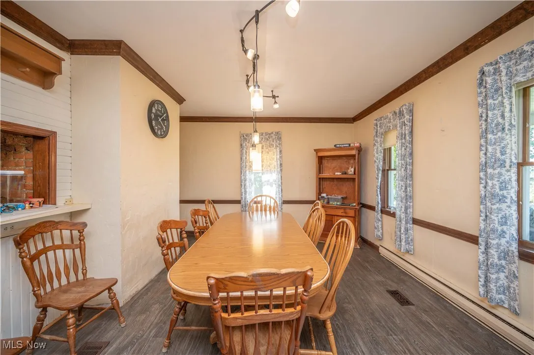 Dining room with baseboard heating, wood finished floors, crown molding, and track lighting